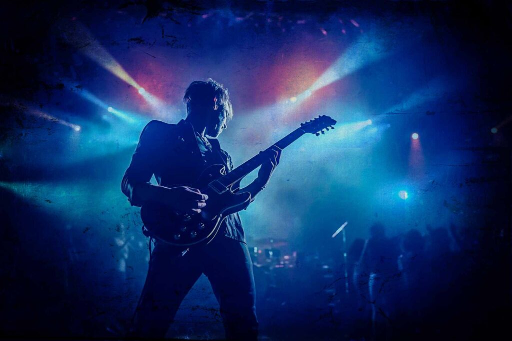 Silhouetted guitarist plays electric guitar on stage under intense colorful lighting during a live concert, creating a perfect moment for social media.