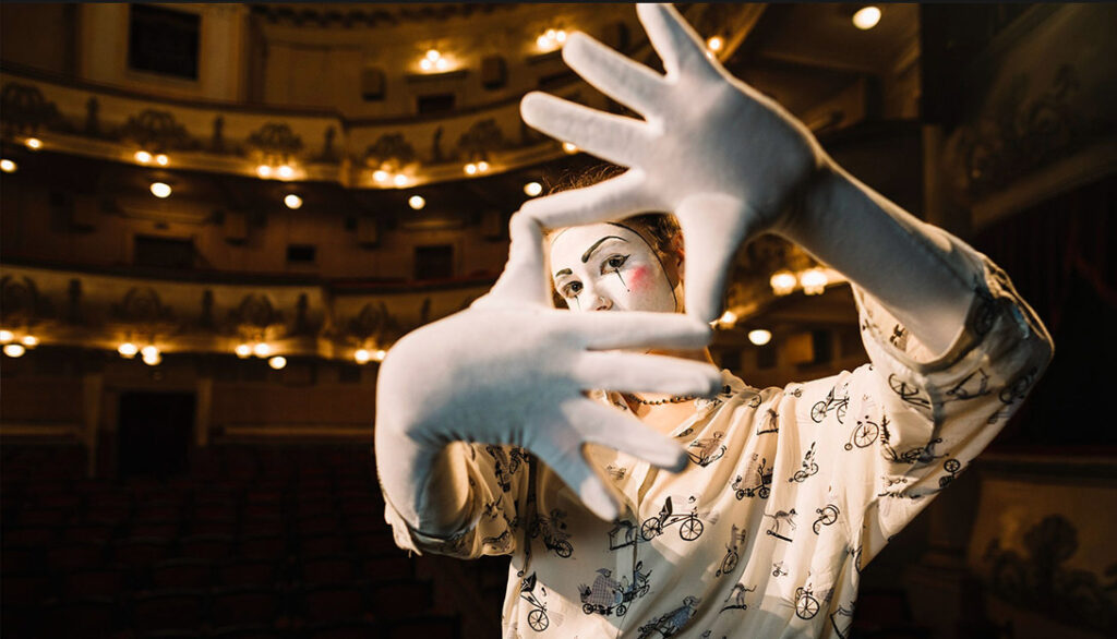 A person with face paint and gloves poses theatrically on a stage in a dimly lit theater, creating the perfect scene for social media design inspiration.