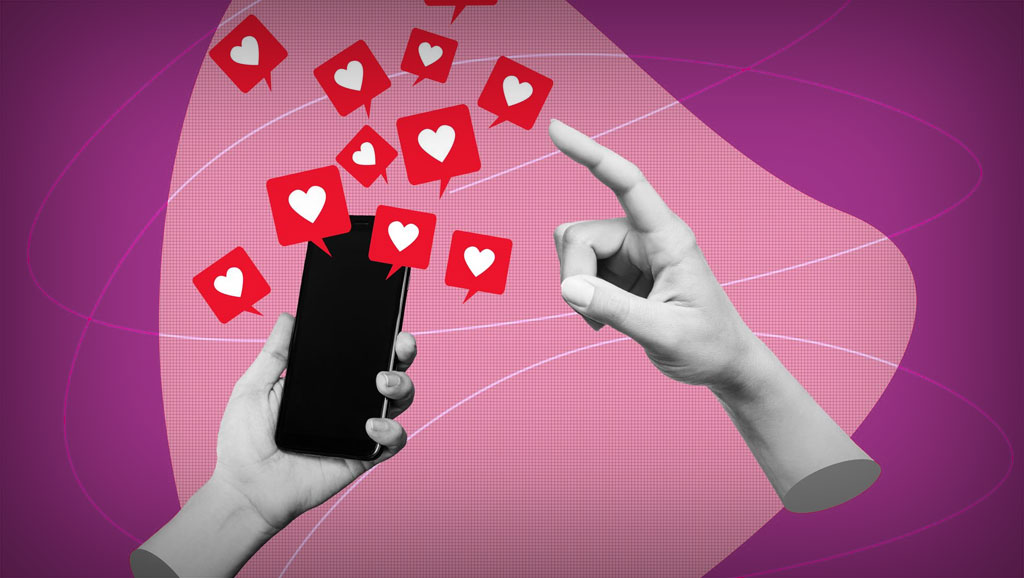 Image of a smartphone held in one hand with red heart notification icons emerging from the screen, reflecting thoughtful social media design. A second hand reaches towards the phone, all set against a pink abstract background.