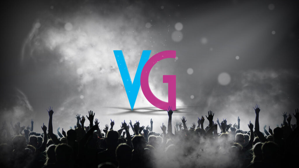 A crowd with raised hands at a concert in front of a misty stage, where large blue and pink letters "V" and "G" are illuminated in the background, creating a mesmerising atmosphere perfect for vibrant marketing opportunities.